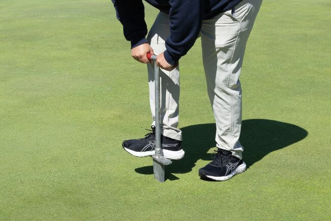 Man drilling a hole into a golf green
